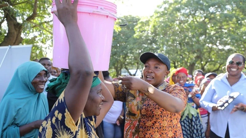 Mkuu wa Mkoa Manyara Queen Sendiga (mwenye kofia), akimtwisha ndoo ya maji makazi wa kijiji cha Gidagabara baada kukabidhiwa mradi wa maji uliotekelezwa  na Shirika la word Vision Tanzania  	na RUWASA. 