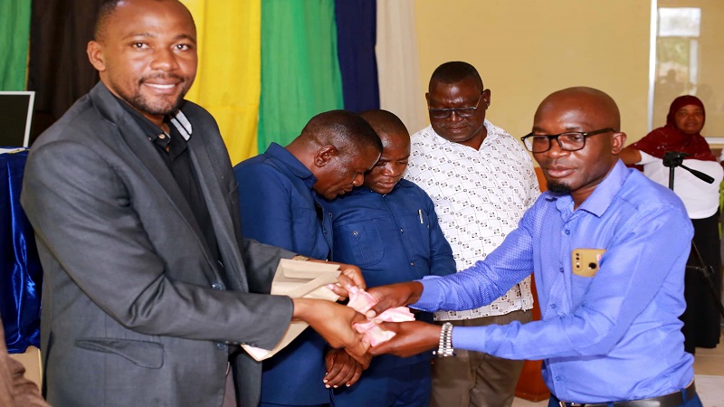 Iramba district commissioner Suleiman Mwenda (L) presents cash to Old Kiomboi ward education officer Daudi Mjungu yesterday after the ward emerged top in the district in the national Standard Seven exams. 