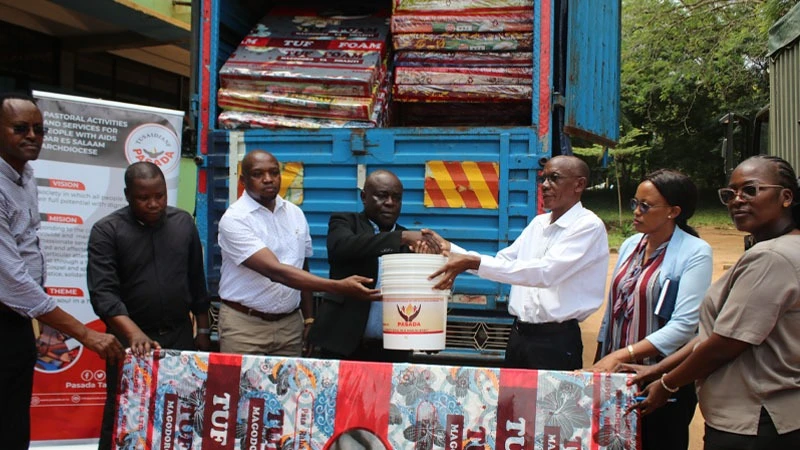 Fr Christian Nyumayo, Pastoral Activities and Services for People with AIDS Dar es Salaam Archdiocese advisory board Chairperson (C) presenting buckets and mattresses worth 8m/- to Kibiti District Commissioner Col Joseph Kolombo (3 rd-R). 