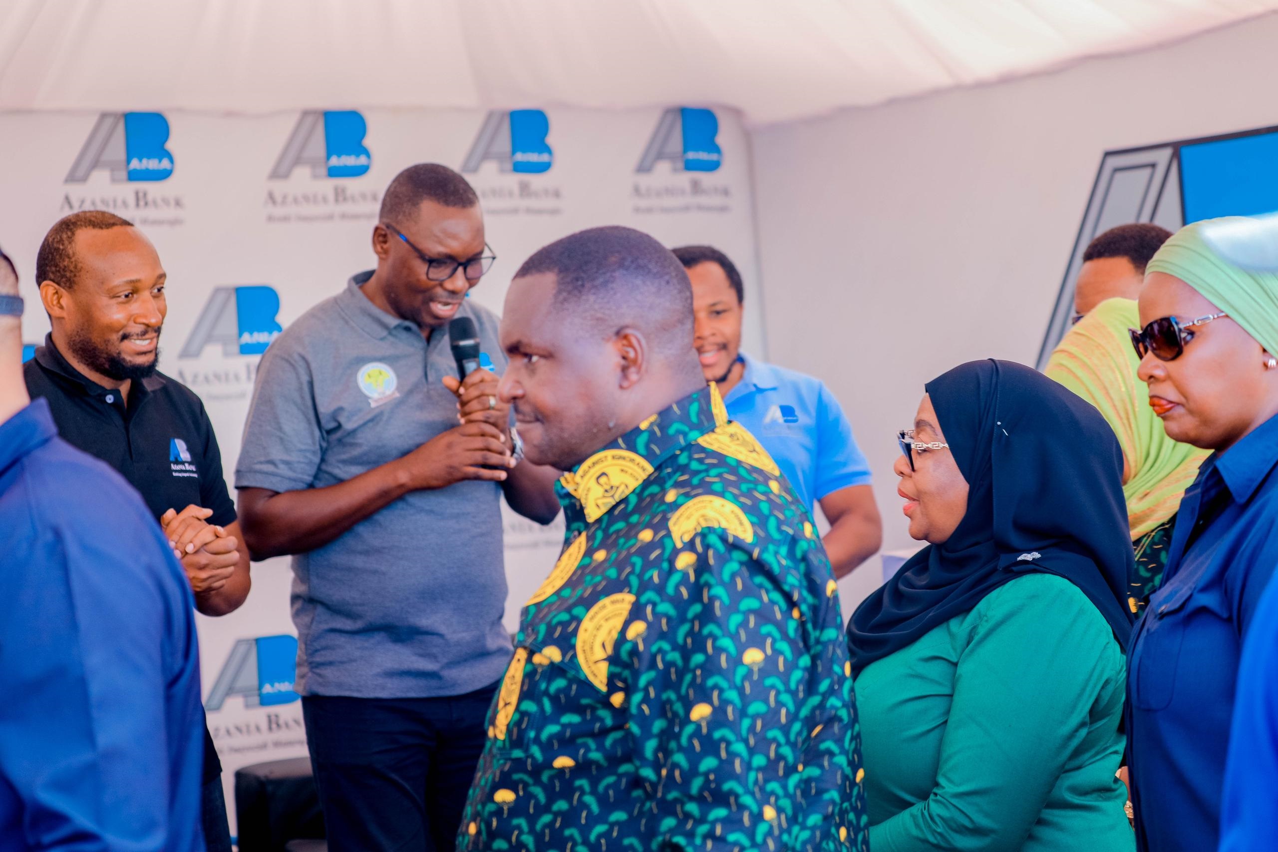 August Matutu (with microphone), Azania Bank Limited’s head of agribusiness, briefs President Samia Suluhu Hassan at the bank’s pavilion at an exhibition to mark Parents Week celebrations held in Katavi Region yesterday. 