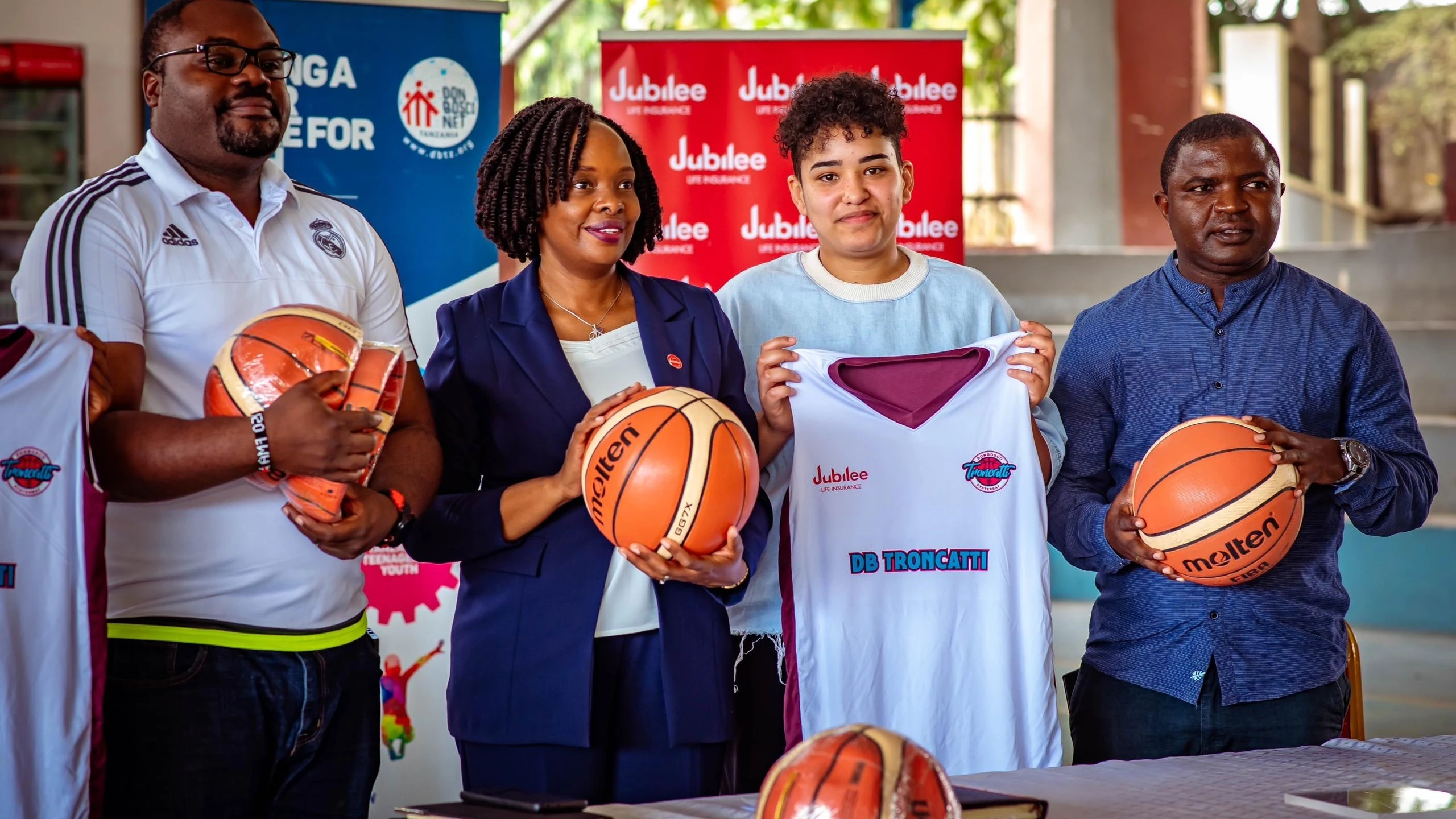 Jubilee Life Insurance Corporation of Tanzania Limited CEO Helena Mzena (2ND-L), Fr Joachim Sivali, (Left) Don Bosco basketball teams Patron, Nadia Samir (2ND-R), Don Bosco Troncatti captain showcasing donated items.