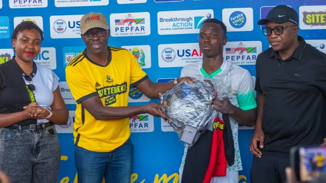 Moses Bateganya, a USAID representative (second left) awards Kassim Hussein who was named the player of the match during the opening of Ndondo Cup tournament in Dodoma between Kikuyu FC and Nkuhungu Terminal FC. 