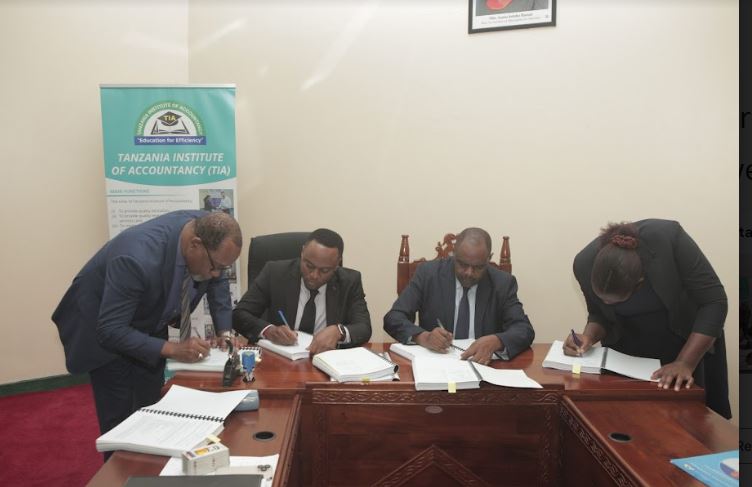 Tanzania Institute of Accountancy (TIA) chief executive officer, Prof William Pallangyo (R) signs documents in Dar es Salaam yesterday with a Salem Construction Co. executive Charles Casmir (sitting, left) for the construction of its Singida campus. 