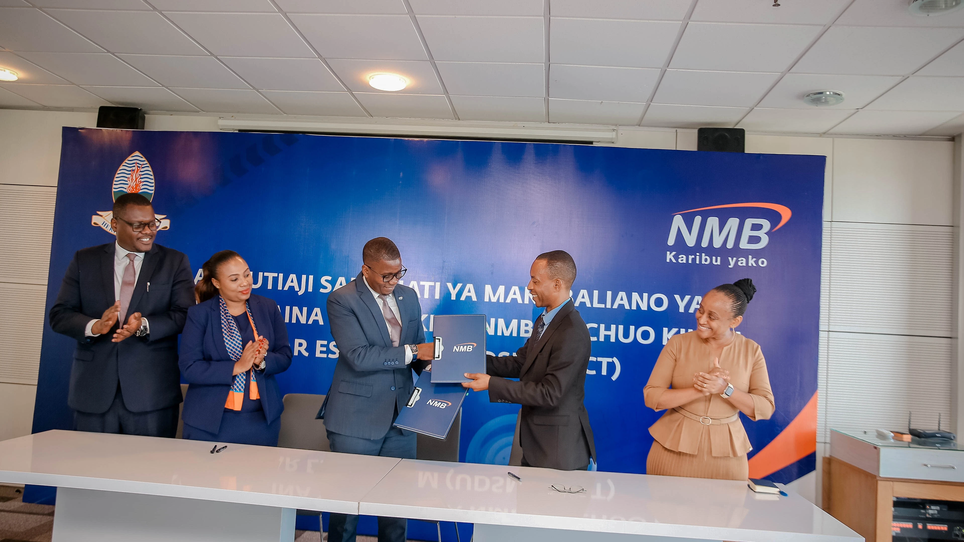 NMB Chief Human Resources Officer, Emmanuel Akonaay (3rd-R) and Deputy Vice-Chancellor of the University of Dar es Salaam (UDSM) in charge of Research, Prof. Nelson Boniface (2nd right), exchanging signed MoU documents 