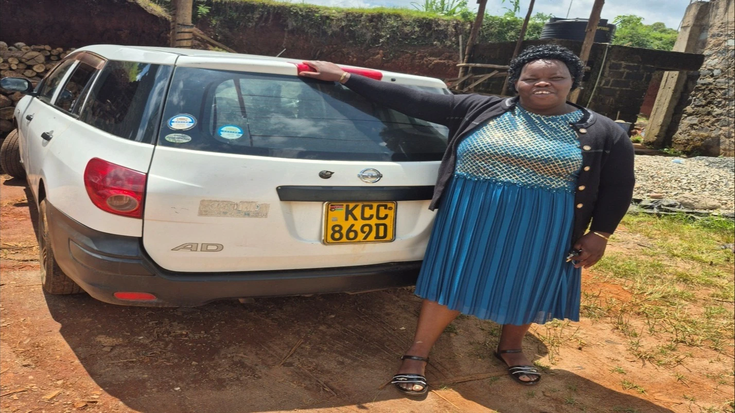 
Parity Wangari standing behind her car

 