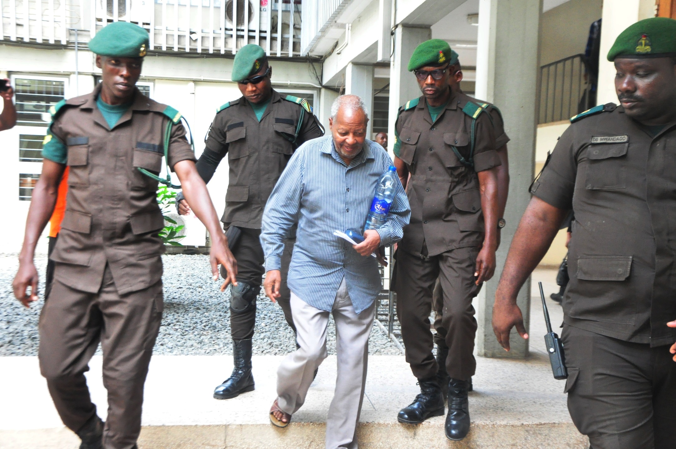 Former Ambassador, Dr. Wilbroad Slaa (C), was under the custody of prison officers as he was escorted out of the Kisutu Resident Magistrate's Court in Dar es Salaam today, heading to remand after being denied bail over charges of publishing false info