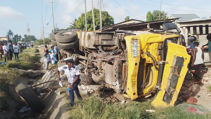 A traffic police officer inspects a lorry which overturned after losing control and collided with three vehicles and four tricycles along Wazo Road slope at Msikitini area in Dar es Salaam yesterday. Residents have expressed concern on the road .