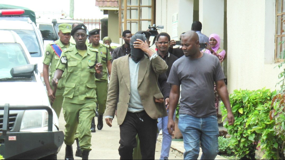 Police Sergeant Rojas Mmali (hiding his face) and militiaman Thomas Mkembela (R) are being escorted by police officers at Iringa District Court on Tuesday shortly before they were charged with the murder of Nashon Kiyeyeu. 