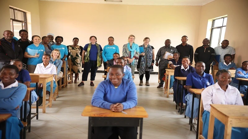 Dr. Lauren Rumble, Associate Director for Gender Equality at UNICEF Headquarters, stands (6 th-R) in the back row of a group photo with UNICEF Tanzania staff, adolescent girls, and members of the Children Protection Committee during a visit to Songwe .