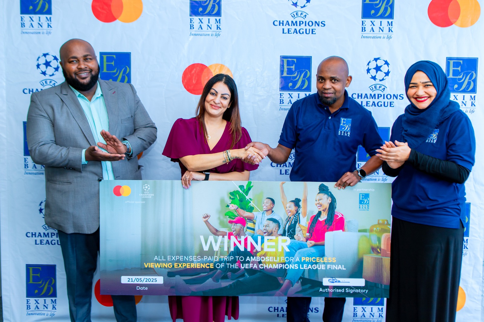 Mshindi kutoka Benki ya Exim Tanzania wa kampeni ya ‘UEFA Priceless’ Manjeet Kaur Mair (wa pili kushoto) akipongezwa na Silas Matoi (wa pili kulia), Mkuu wa Idara ya Huduma Mbadala za Kidijitali wa Exim katika kampeni ya matumizi ya Exim Mastercard